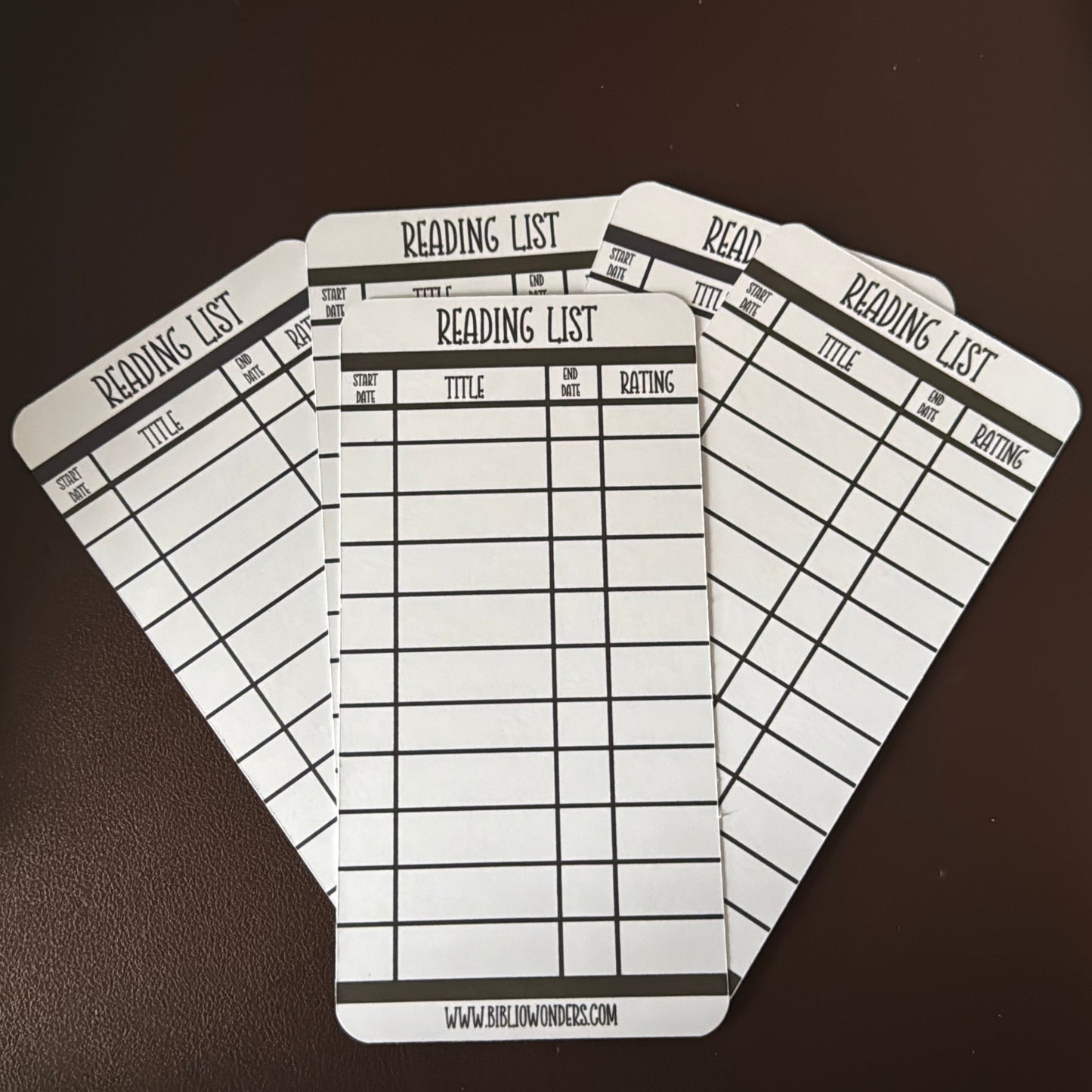 Four identical reading list bookmarks on a dark surface